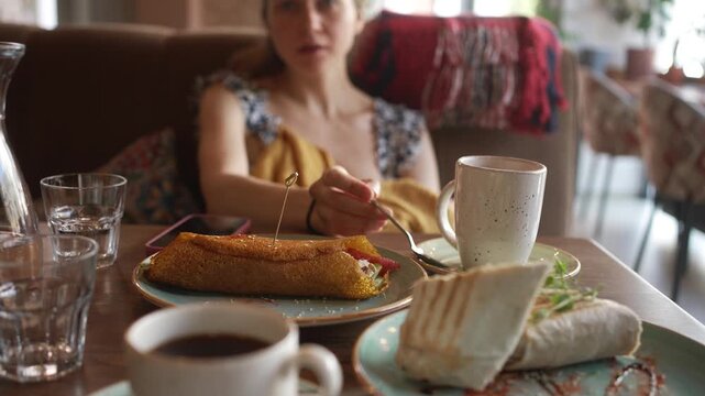 Busy mother hastily eats her lunch in a cafe, glancing around anxiously as she multitasks during her limited break, a poignant look at the demanding reality of motherhood