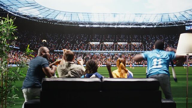 Football fans watch a match on the sofa with snacks and drinks ready for game night as high fidelity sports broadcast brings stadium crowd energy home.