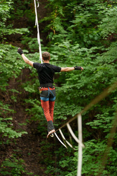 Man walking highline with safety leash above forest canopy with arms outstretched, extreme sport courage and conquering fear at height concept.