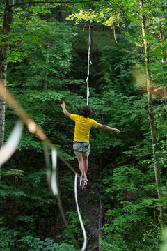 Slacklining highline walking balancing forest athlete extreme sport risk challenge motivation focus yellow shirt