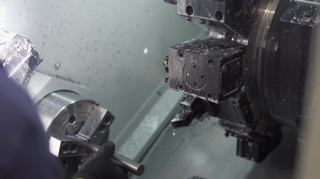 Technician in gloves operates CNC lathe, adjusting and monitoring metal machining in bright, controlled workshop. Clean, focused, industrial process.