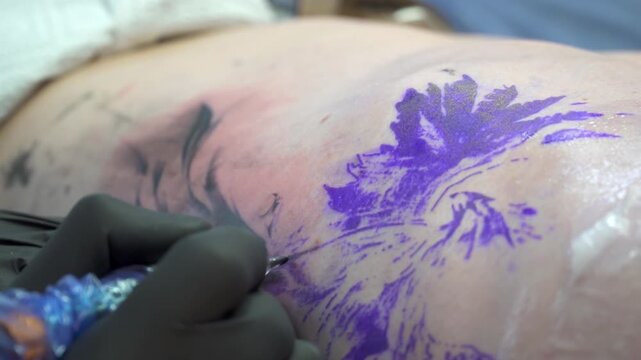 Close-up shot of a tattoo artist with black gloves inking a detailed floral outline on skin, capturing hand movement, color, and fine linework.