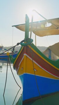 Vivid luzzu fishing boat floats calmly in sunlit harbor, shot in stunning vertical video, ideal for mobile, stories, and social media reels.