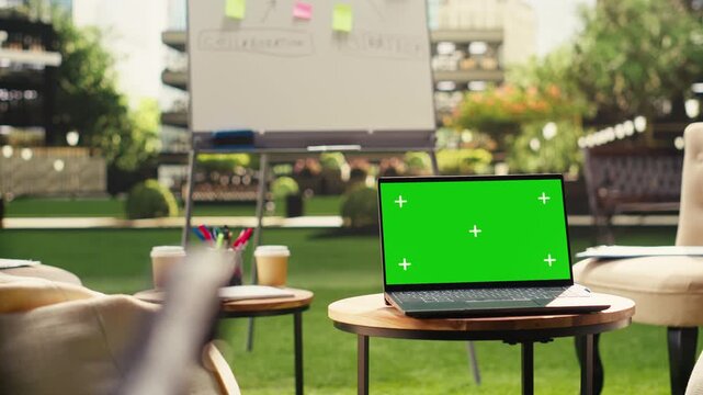 Isolated green screen on laptop in sunlit office terrace with no people, device on round table with chroma key and screen replacement.