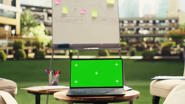 Chroma key mockup laptop on round table near lounge chairs, modern urban rooftop workspace with editable screen on device, informal meeting area work environment, for screen replacement.