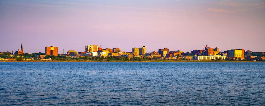 Sunset light over the Portland, Maine skyline seen across Back Cove, with calm blue water and pastel evening sky.