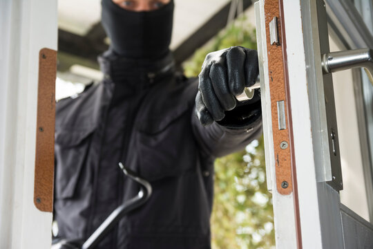 A male burglar opens a house door with a crowbar during daytime