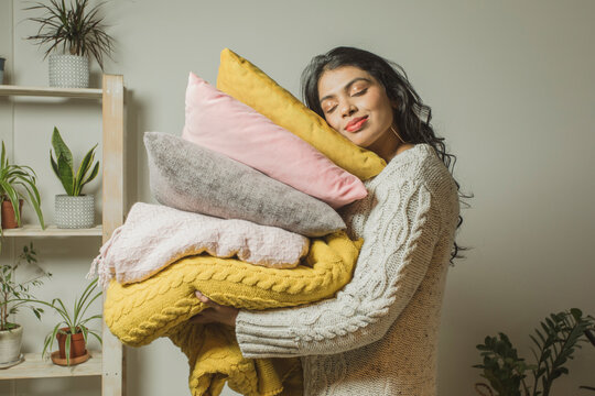 Woman with eyes closed carrying pillows and blankets at home