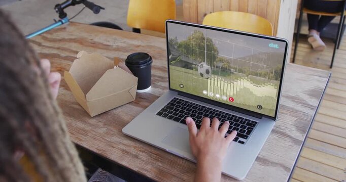 Adult male reacting to laptop audio bars, snacking from takeout box and typing at cafe table