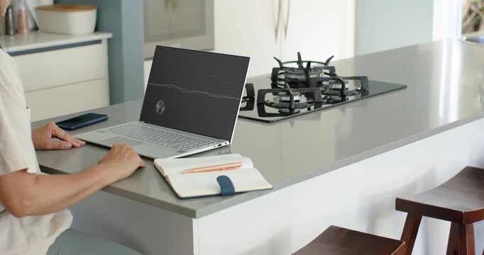 Mature woman 45-55 sitting in kitchen watching emerging animation on laptop, tracking red climber