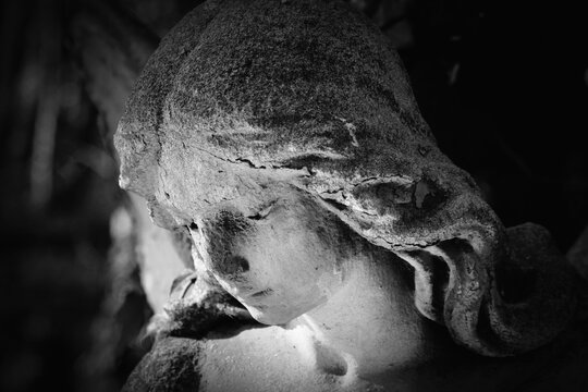 Close-up of a weathered stone angel with bowed head in black and white, expressing sorrow, remembrance, silence, and eternal peace.