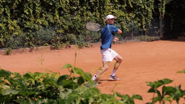 Male tennis player returning forehand shot during outdoor clay court rally. Concept of tennis competition, athletic performance, fast reactions, precision, endurance and sports training.