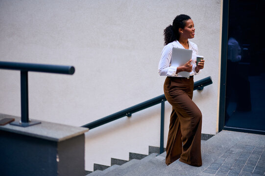 Confident African American Business Woman Walking Up Stairs With Laptop And Coffee Cup