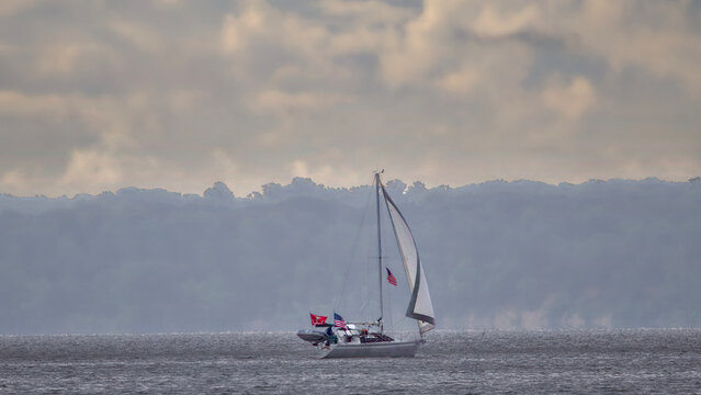 Small sailboat crossing misty gray water
