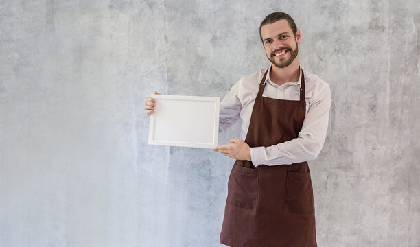 Caucasian barista man wearing an apron holding a blank white sign, perfect for promotions, announcements, advertising, and customizable marketing messages