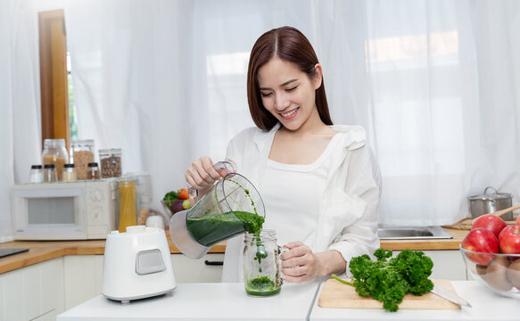 Smiling young asian woman preparing green smoothie in a modern kitchen with vegetables apples for healthy nutrition wellness.vegan woman eating healthy food and tasty food health care