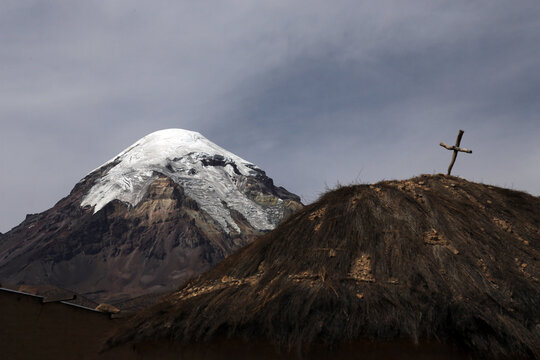 Snowcapped volcano Sajama with straw house with cross in foreground, Sajama National Park, Bolivia