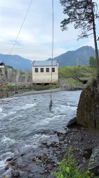 Rushing rapids of a mountain river cascade past the historic stone building and dam of the Chemal hydroelectric power station under a cloudy sky, 4k