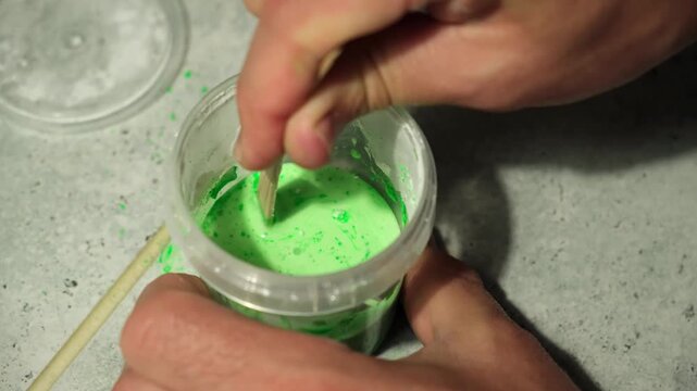 A chemical experiment for the production of a non-Newtonian liquid. A child mixes white powder and green food dye in a plastic container on a table. DIY slime kit, creative hobby, home activity.