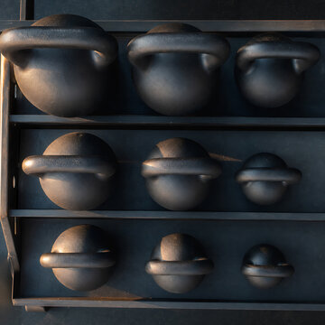 Row of matte black kettlebells stored on a steel rack, overhead view