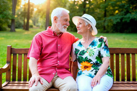 Senior Caucasian couple sitting closely on park bench, embracing and smiling at each other, expressing lasting relationship and retirement lifestyle. Ideal for senior care, insurance
