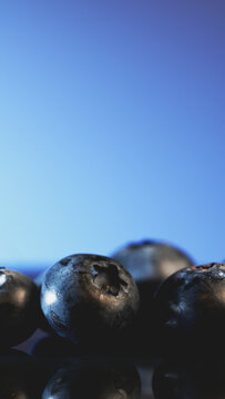 Macro shot of fresh blueberries with reflection on glass surface. Juicy berries on blue background for healthy food blog, social media stories template, mobile wallpaper, and wellness advertising.