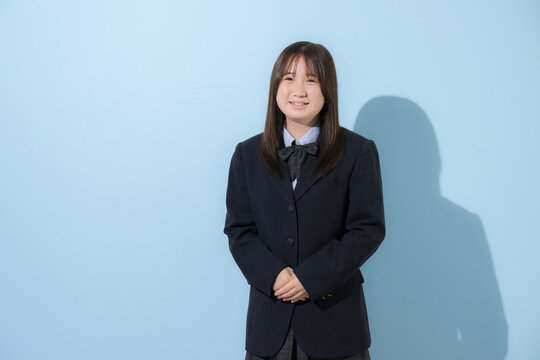 水色背景で制服で立つカメラ目線笑顔の女子中学生や高校生のイメージ	