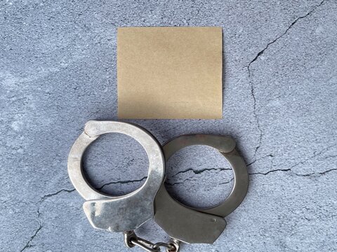 Handcuffs with blank sticky note on concrete background symbolizing justice, crime prevention, legal message and copy space.