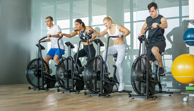Group of multiethnic young people cycling together on airbikes in a modern gym