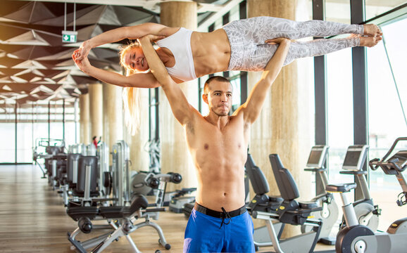 Strong male acrobat lifting and balancing a female partner high in gym interior
