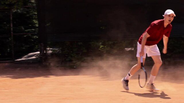 Male tennis player in red shirt returning forehand shot on outdoor clay court. Concept of sports apparel marketing, active leisure, premium tennis equipment and recreational activities.