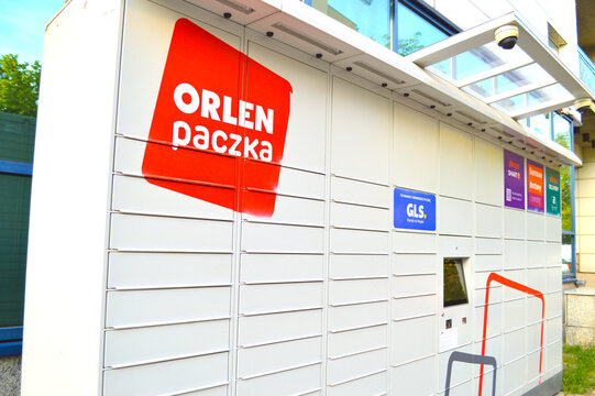 Modern white Orlen Paczka automated parcel locker machine with red logo on a city street in Poland for easy shipping and package collection.