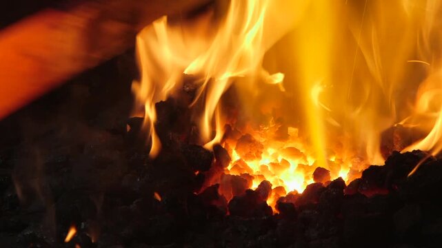 Extreme close-up of a red hot steel bar being moved through glowing coals inside a traditional blacksmith forge during the forging process.