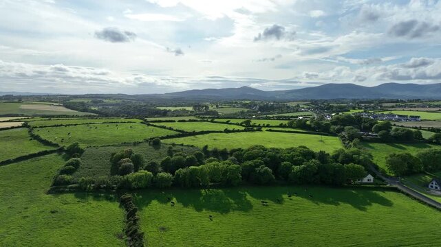 Aerial evening light green lush farmland wooded forests patchwork fields and distant mountains Rural Waterford Ireland summer evening
