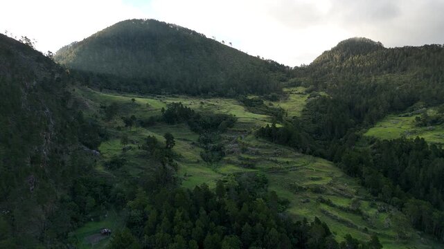 aerial drone footage of receding mountain ridgelines fading into hazy silhouette under a dramatic, cloud-heavy sunset sky in Constanza, Dominican Republic.