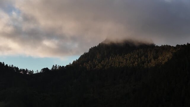 Cinematic aerial drone footage of receding mountain ridgelines fading into hazy silhouette under a dramatic, cloud-heavy sunset sky in Constanza, Dominican Republic.