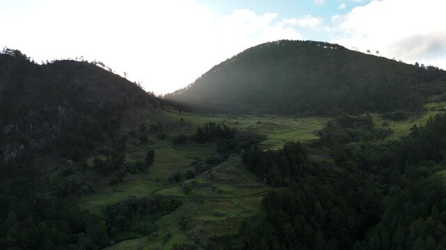 Cinematic aerial drone footage of receding mountain ridgelines fading into hazy silhouette under a dramatic, cloud-heavy sunset sky in Constanza, Dominican Republic.