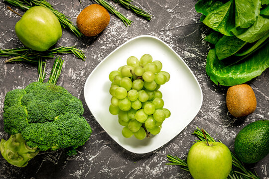 green fresh vegetables and fruits for healthy salad on dark table background top view