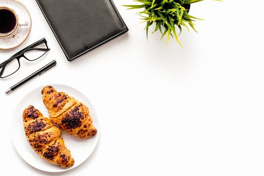 Light breakfast of businessman. Coffee and croissant near notebook and glasses on white background top view copy space