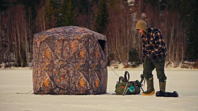 A Man With A Portable Ice Tent And Backpack During Winter Ice Fishing. Static Shot