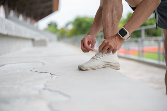 Close up of a man's hands tying sneaker shoelaces on concrete stairs in sports stadium.