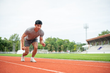 Fototapeta premium Asian athletic man launching from start line on running track in sports stadium.