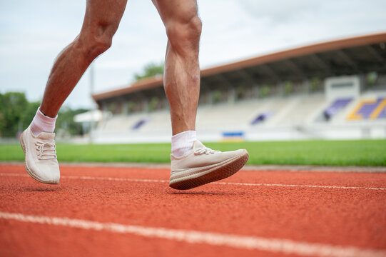 Close up of a male runner's legs and feet wearing sneakers running on a track in sports stadium.