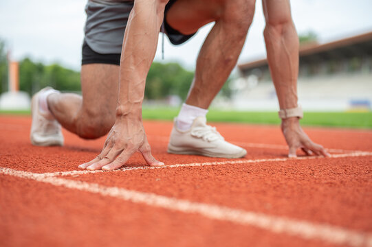 Close up of male sprinter's hands and feet in starting position on running track in sports stadium.