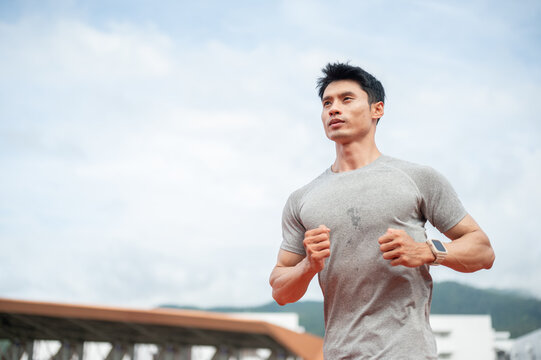 Low angle of an asian athletic man running or jogging during an exercise session in sports stadium.