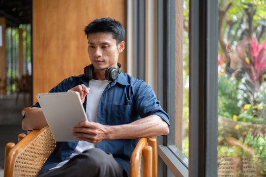 Asian man artist using tablet with stylus pen while working on a design at table the in cafe.