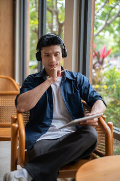 Asian professional artist man with headphones using tablet with stylus while working in the cafe.