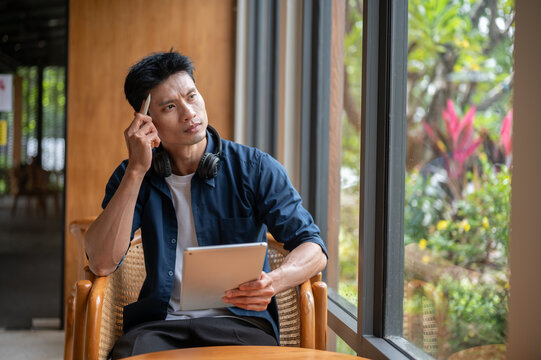 Thoughtful Asian entrepreneur looking away while holding tablet in cafe.