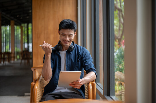 Asian artist man smiling looking at tablet and making a fist in excited while working in the cafe.