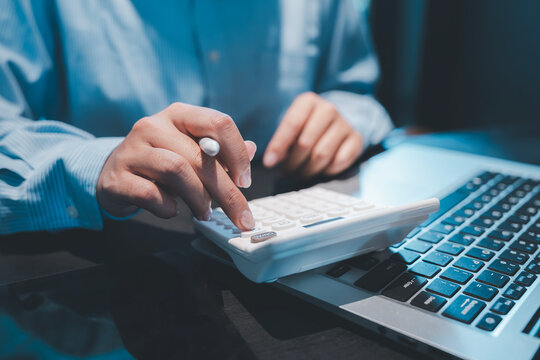Financial accounting and tax preparation concept close up of accountant hands pressing white calculator buttons and holding pen near laptop for evaluating business cost expense and budget estimate